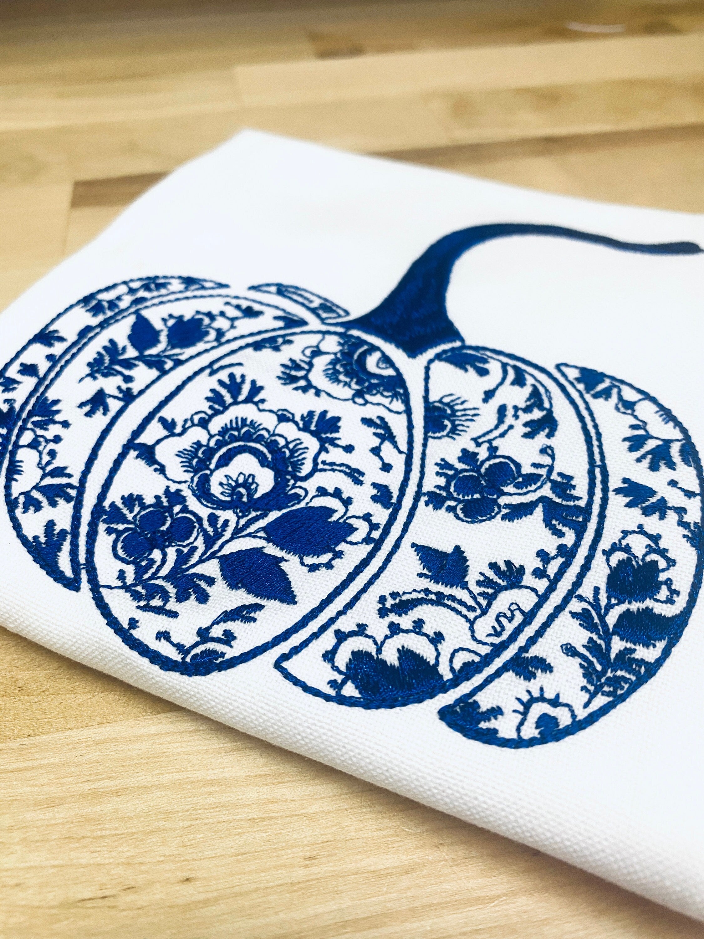 Closeup photo of a chinoiserie pumpkin towel embroidered on a white cotton tea towel showing detail of stitches.