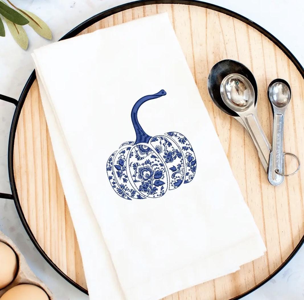 Chinoiserie decor blue and white pumpkin on a white tea towel laying on top of a wood and iron serving board with measuring spoons and eggs on the side. Ready for fall!