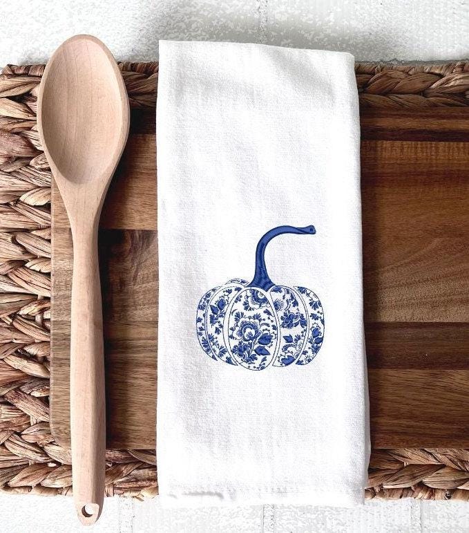 Chinoiserie pattern pumpkin in blue and white on a cutting board with a wooden spoon laid on top of a wicker placemat