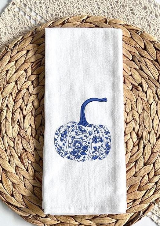 Chinoiserie blue and white pumpkin fall decor embroidered tea towel set on a woven placemat over a crochet throw.