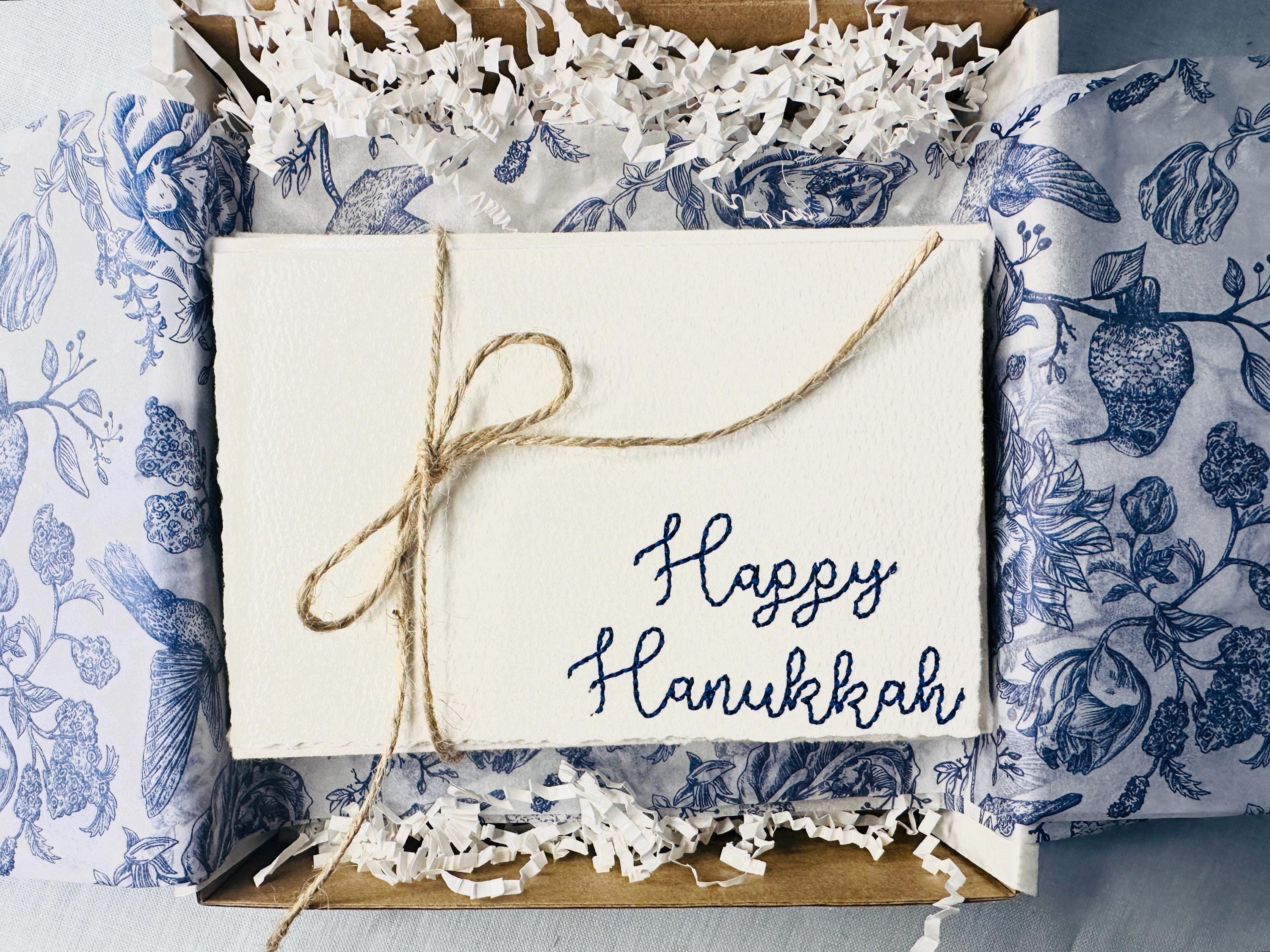 Set of 4 embroidered cards in blue with Happy Hanukkah. Cards are bundled with twine and prepared for gifting set in a white box with white crinkle paper and blue and white chinoiserie tissue.