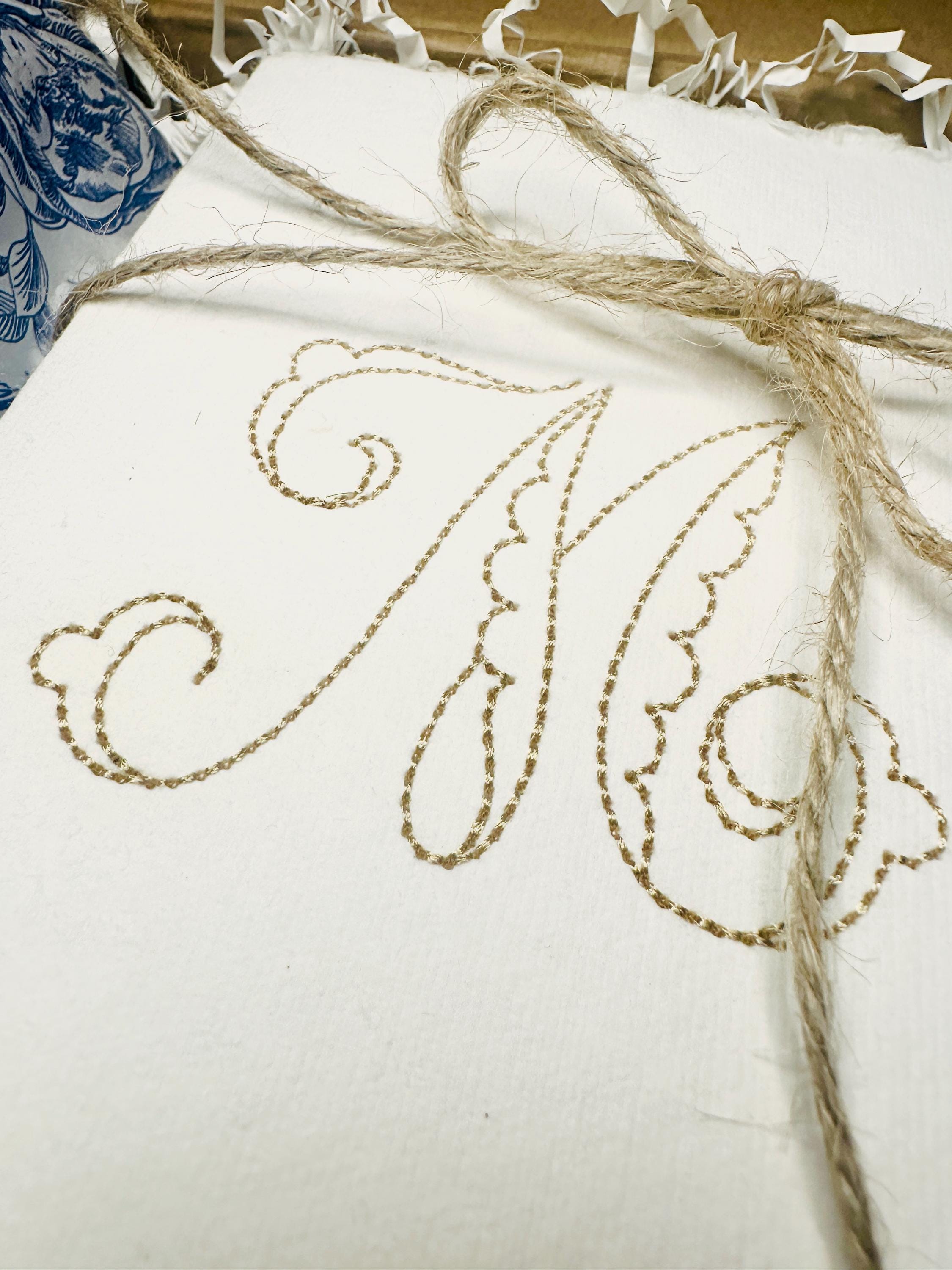 A close up of a custom note card stationery personalized with an initial M tied in twine on chinoiserie blue and white tissue.