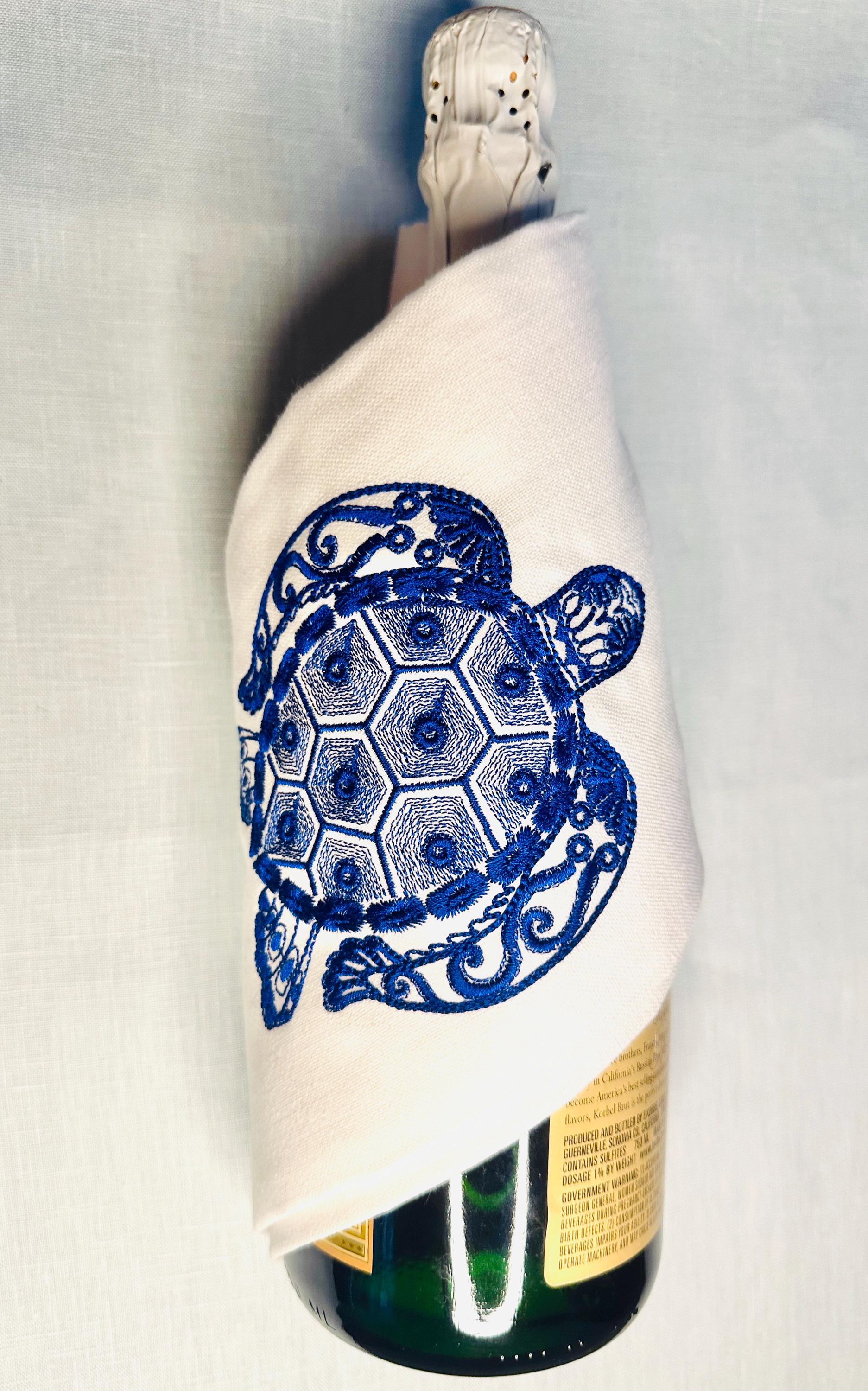 Ocean themed gift of a sea turtle embroidered on a white tea towel and wrapped around a champagne bottle ready for the party!