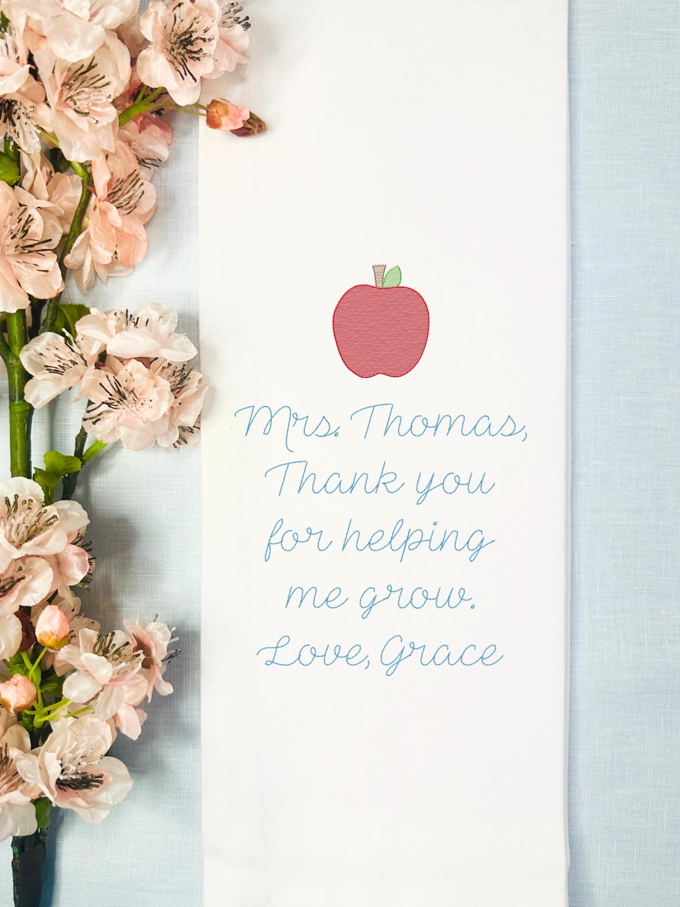 Teacher gift of embroidered tea towel with message to teacher set on a blue linen tablecloth with an apple embroidered on top.