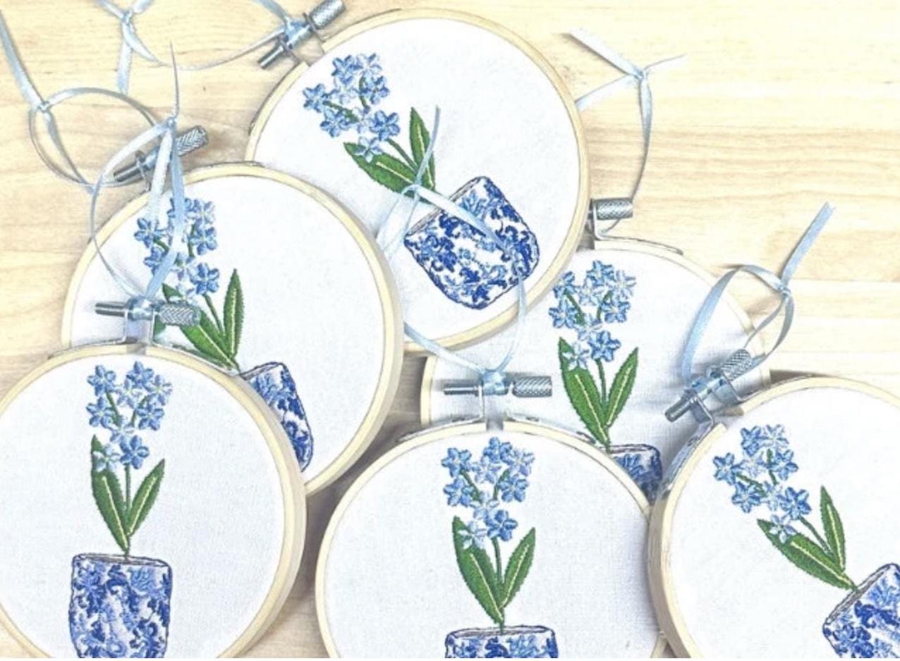 A bulk order of six of the blue flowers in chinoiserie pots with blue ribbons set on a wooden background waiting to be shipped. You receive only one with an order.