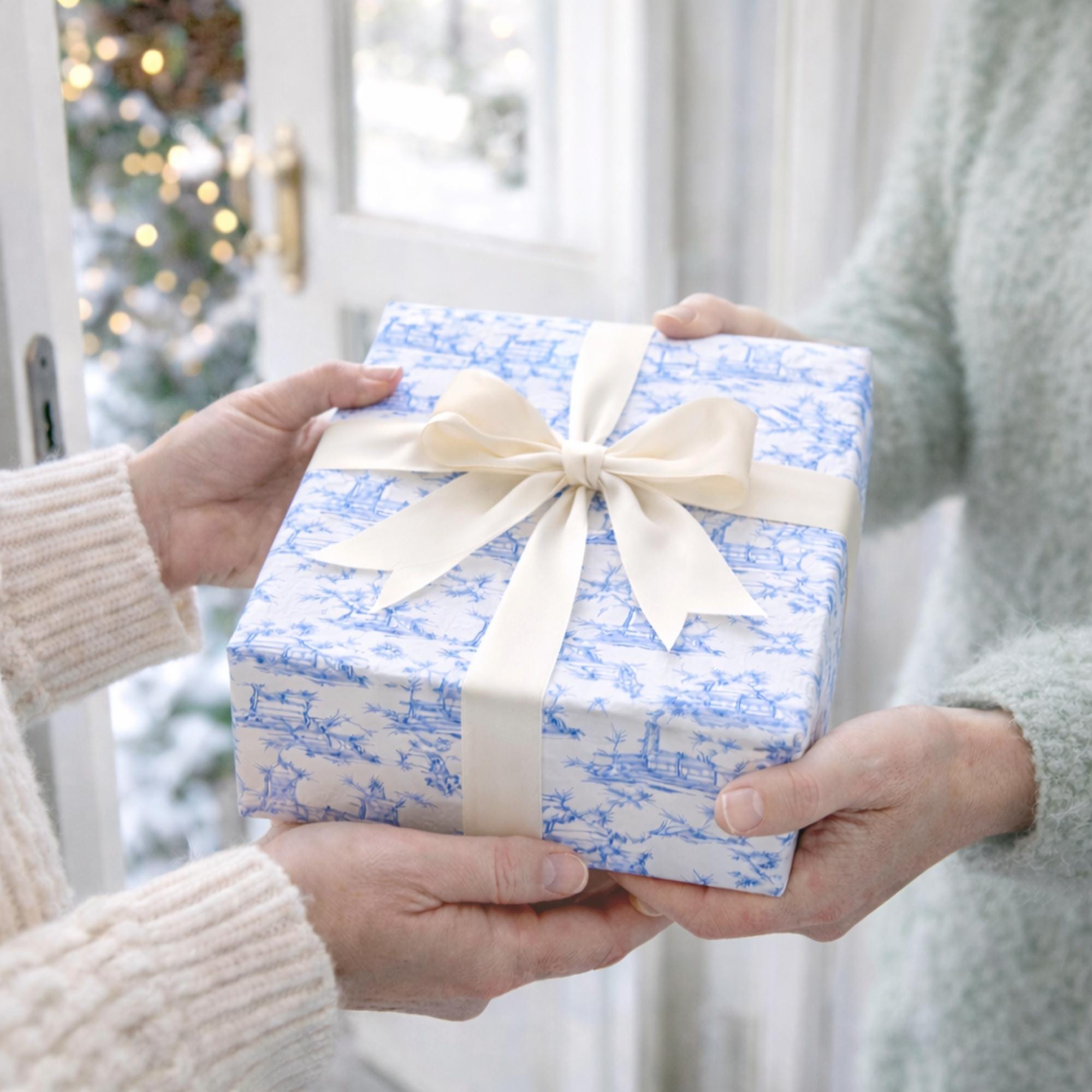 Woman handing another woman a hostess gift wrapped in blue and white paper with a bow.