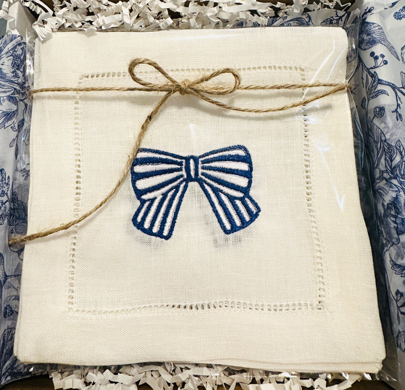 An embroidered linen cocktail napkin with a blue and white bow