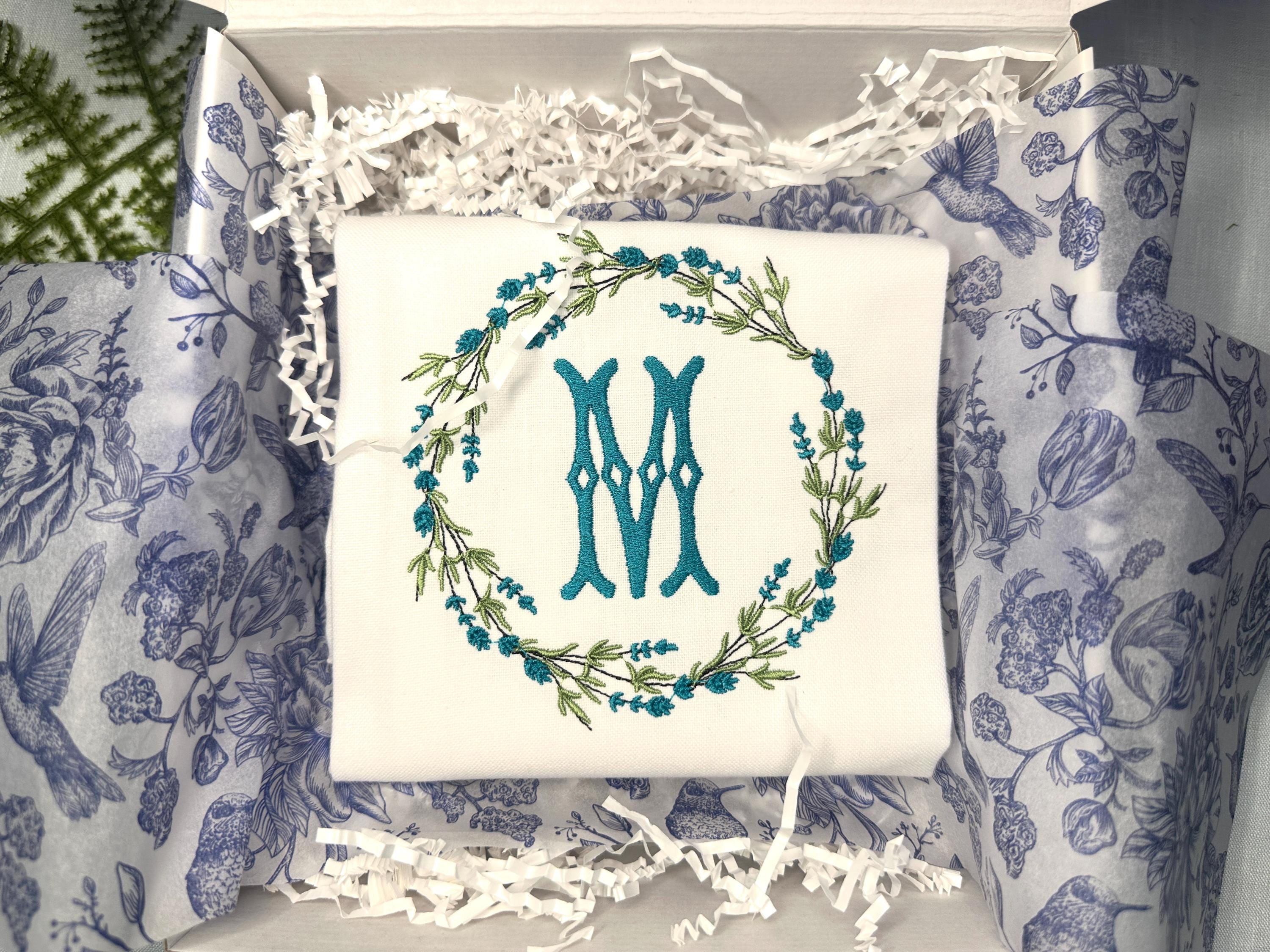 A housewarming gift embroidered towel with a teal wreath and letter M.