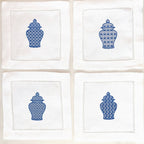Set of four white linen napkins each with a slightly different chinoiserie design stitched in blue on each. They are set on a white background.