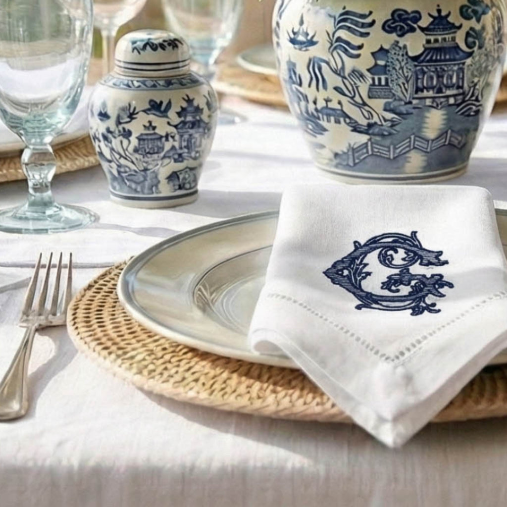 Table setting with blue and white ceramic jars, a napkin with a monogram, and cutlery on a light surface.