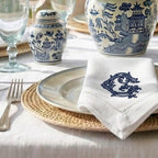 Table setting with blue and white ceramic jars, a napkin with a monogram, and cutlery on a light surface.