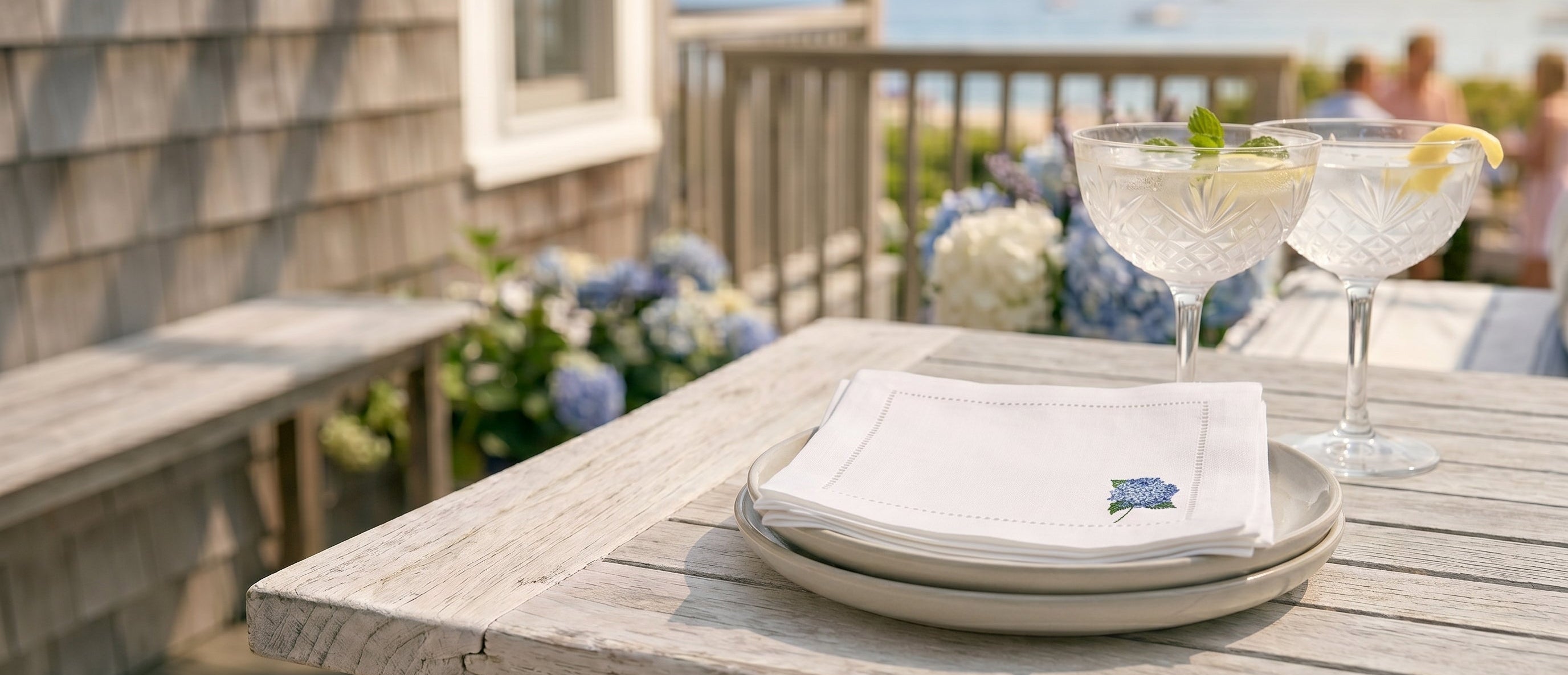 Table setting with glasses and a napkin on a deck overlooking the ocean.