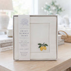 Sweet Humble Home embroidered cocktail napkins set in a gift box displayed on a wooden table in a bright, softly blurred home interior.