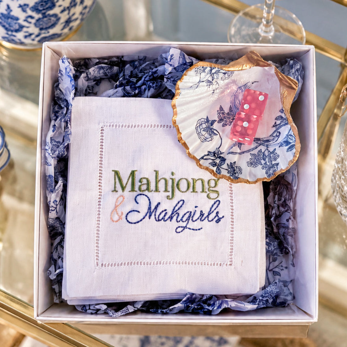 4 Mahjong & Mahgirls embroidered cocktail napkins in a gift box with a chinoiserie shell dice chip and two pink dice on a bar cart.