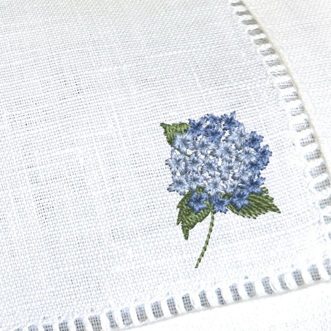 White napkin with embroidered blue flower design on a dark surface
