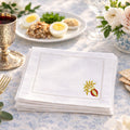 Stack of white napkins with a pomegranate embroidered on a table setting with food and decor.