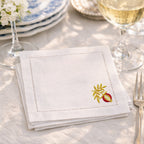 White embroidered pomegranate cocktail napkin on a table setting with wine glasses and cutlery.