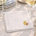 White napkin with embroidered design on a table setting with wine glasses and plates.