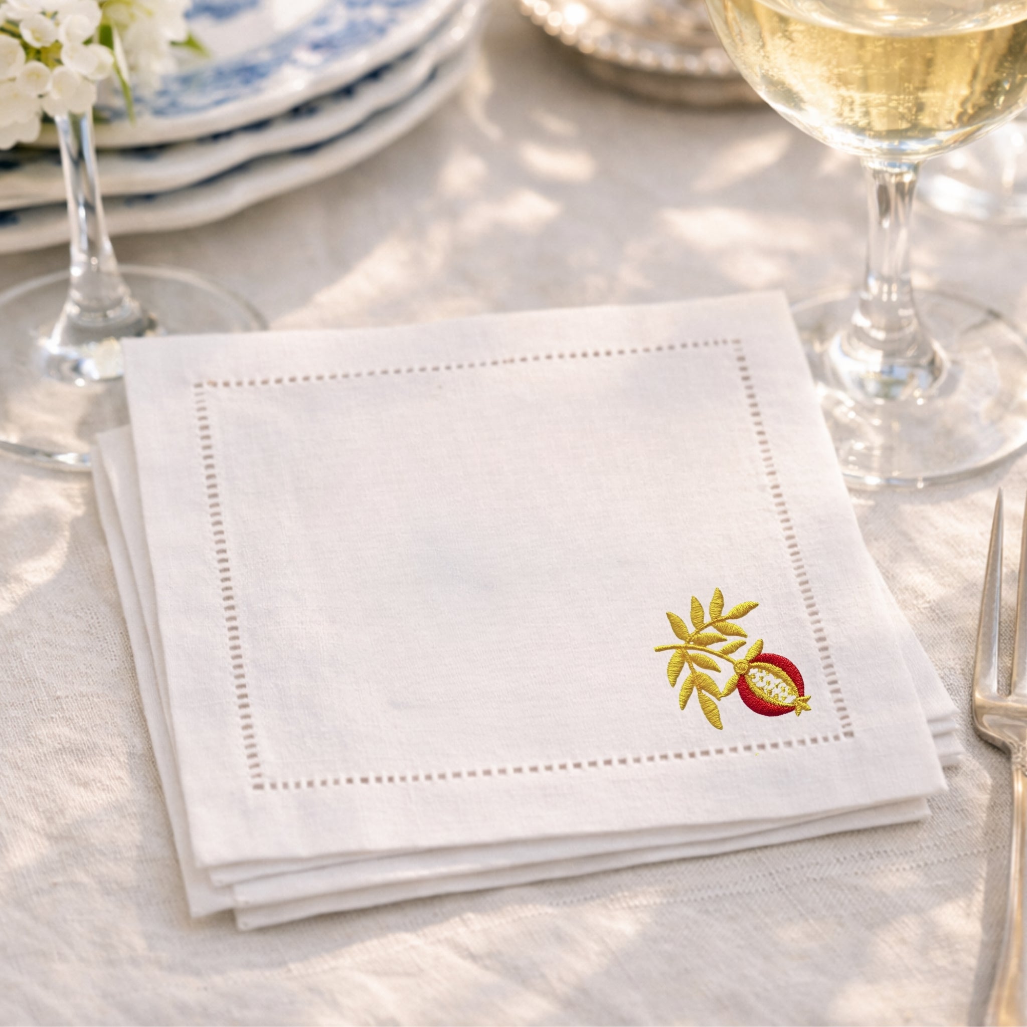 White napkin with embroidered design on a table setting with wine glasses and plates.