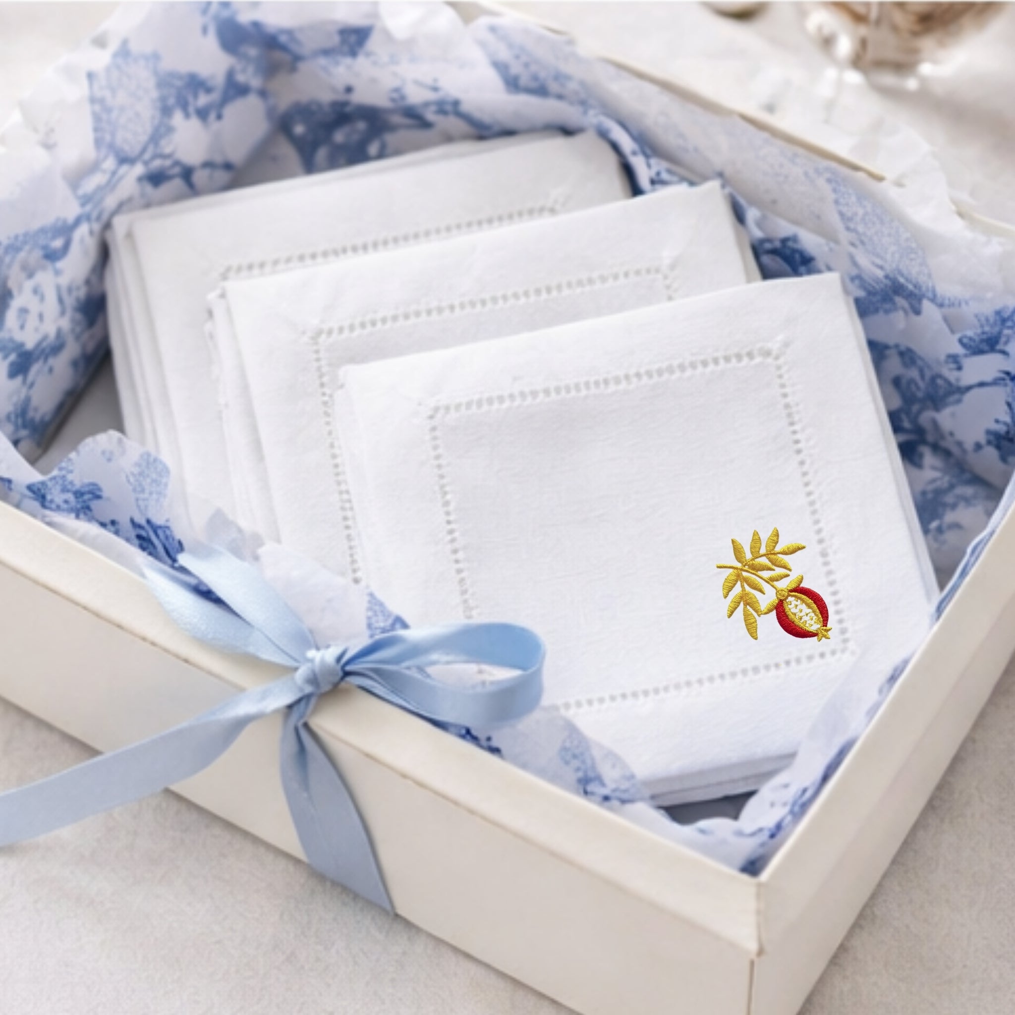 Three sets of 12 White embroidered coasters with an embroidered pomegranate in a decorative box with blue ribbon.