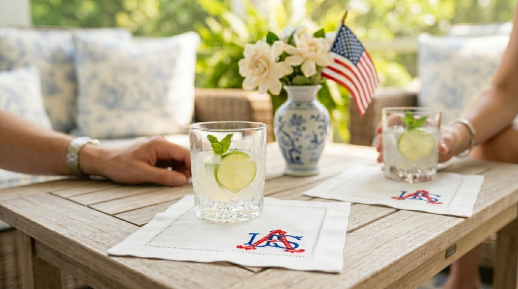 Two glasses with lime wedges on a table with American flags and floral arrangements white linen cocktail napkins with USA embroidered in the right bottom corner.