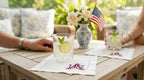 Two glasses with lime wedges on a table with American flags and floral arrangements white linen cocktail napkins with USA embroidered in the right bottom corner.