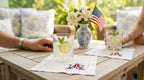 Two glasses with lime wedges on a table with embroidered cocktail napkins with USA embroidered in the bottom right corner, American flag, and flowers.