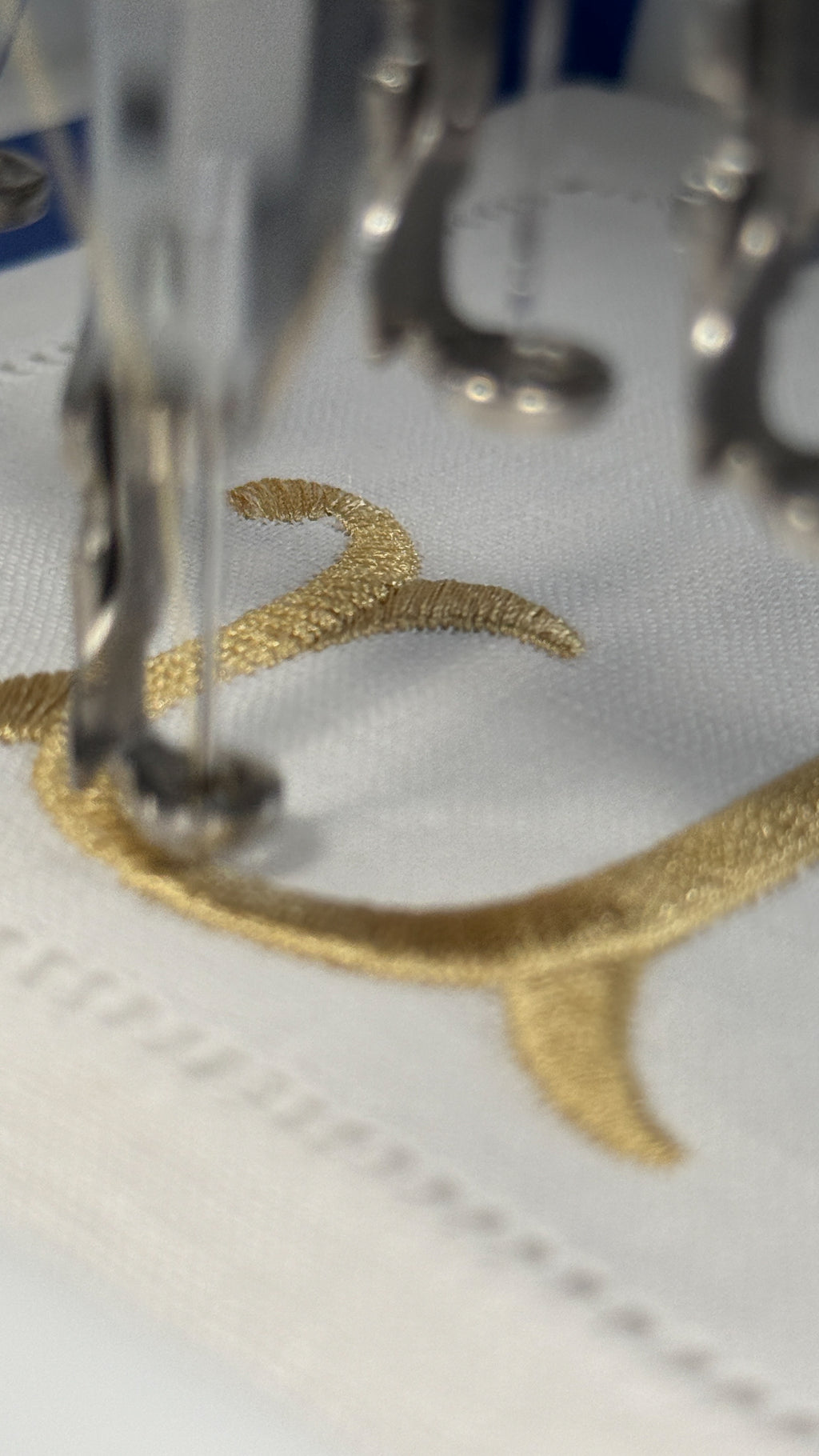 Close-up of a sewing machine needle stitching gold thread on fabric