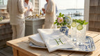 Outdoor setting with a table displaying a book, glasses with drinks, and a vase with flowers.