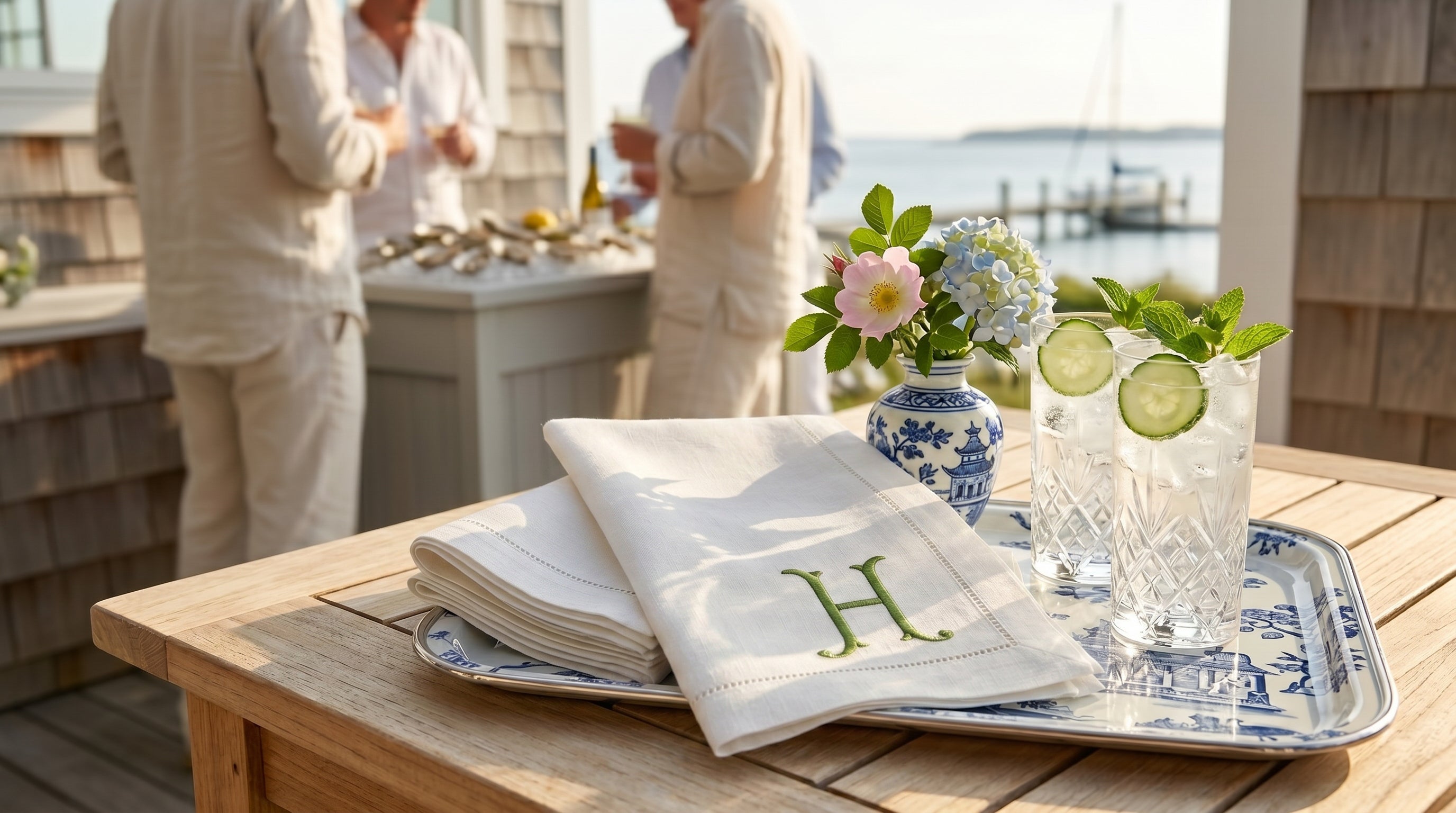 Outdoor setting with a table displaying a book, glasses with drinks, and a vase with flowers.