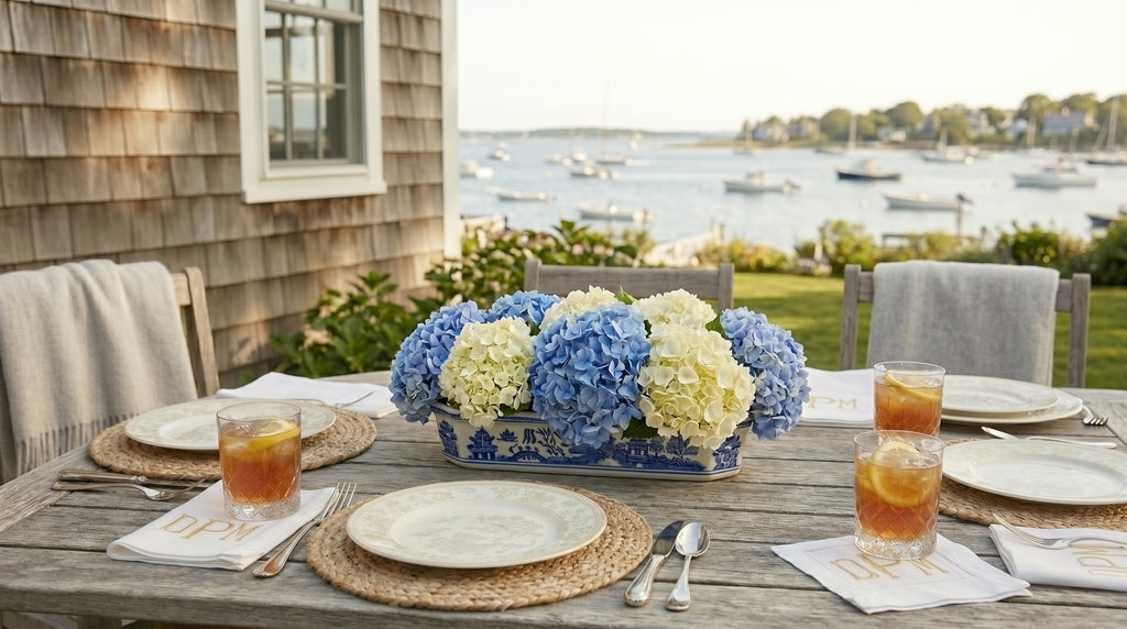 Outdoor dining table set with a floral centerpiece, glasses of iced tea, and views of a harbor.