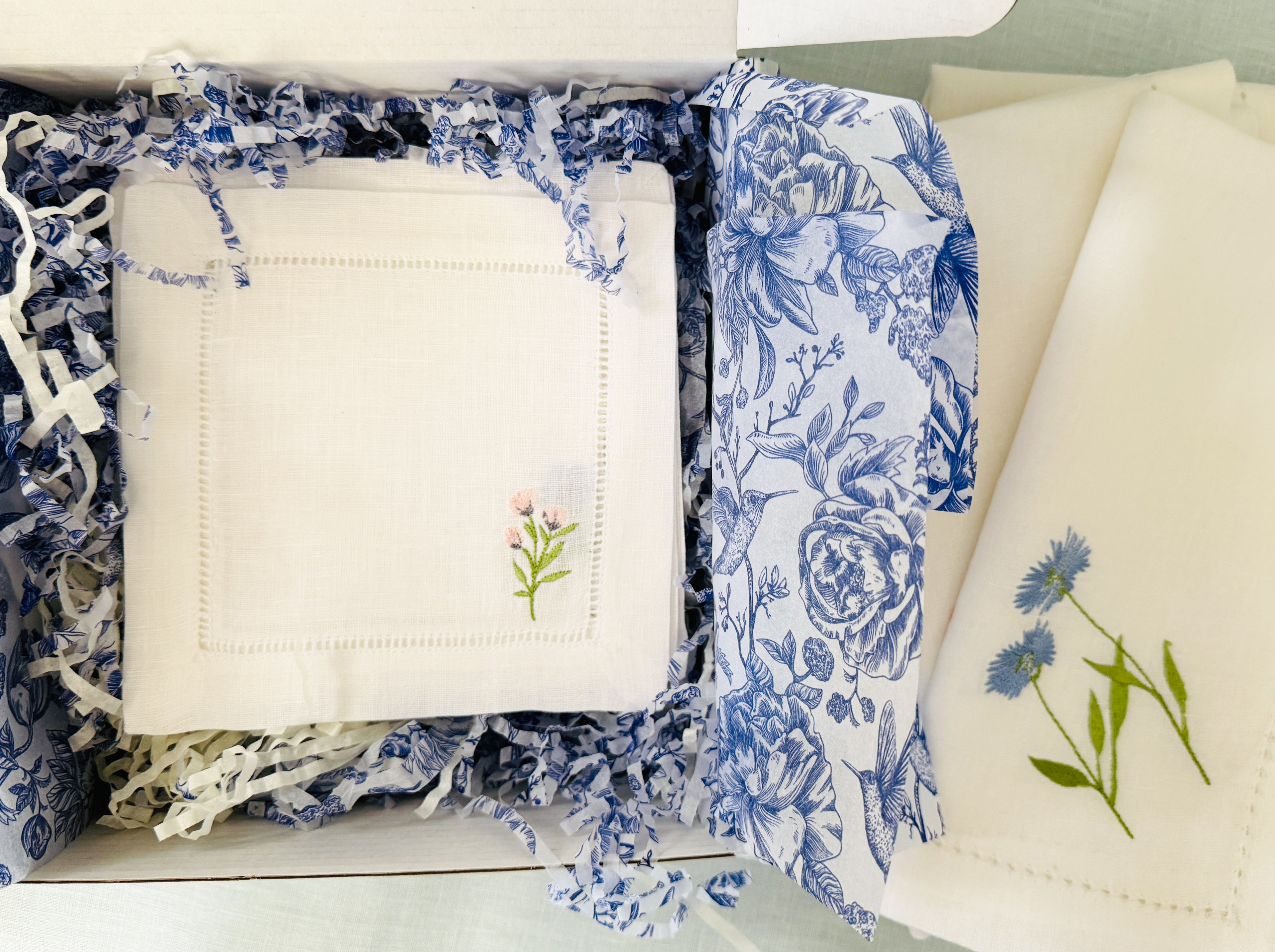 stack of linen cocktail napkins in a gift box. The napkin showing is a small pink flower with a napkin from the wildflower dinner napkin to the right.