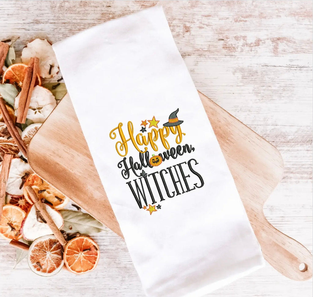 A white tea towel on a light wood cutting board embroidered with the words Happy Halloween Witches with a fall-inspired potpourri at the end of it.