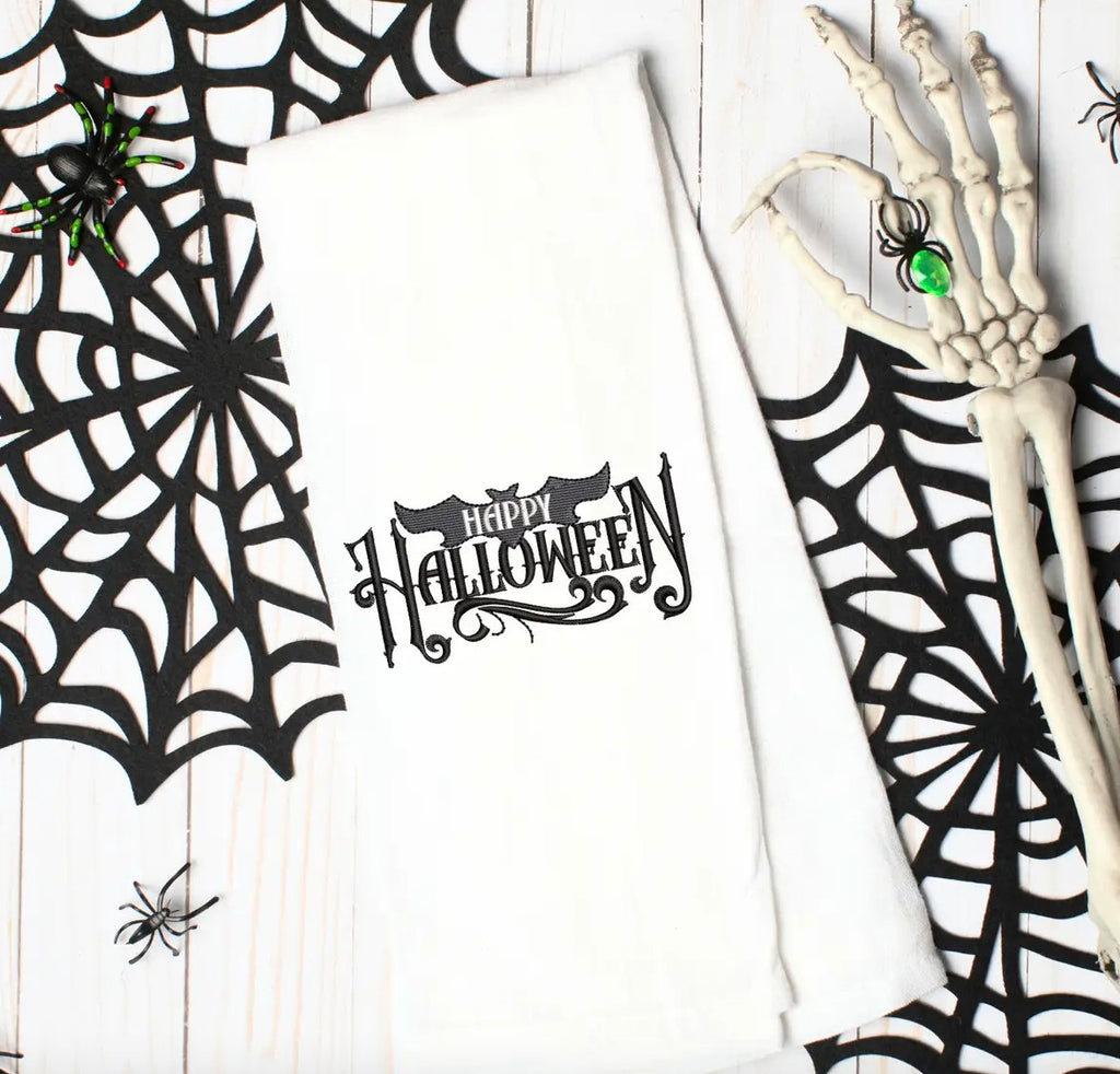 A white kitchen towel with the words &#39;Happy Halloween&#39; embroidered in black with a decorative font and a bat design.
