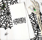 A white kitchen towel with the words &#39;Happy Halloween&#39; embroidered in black with a decorative font and a bat design.