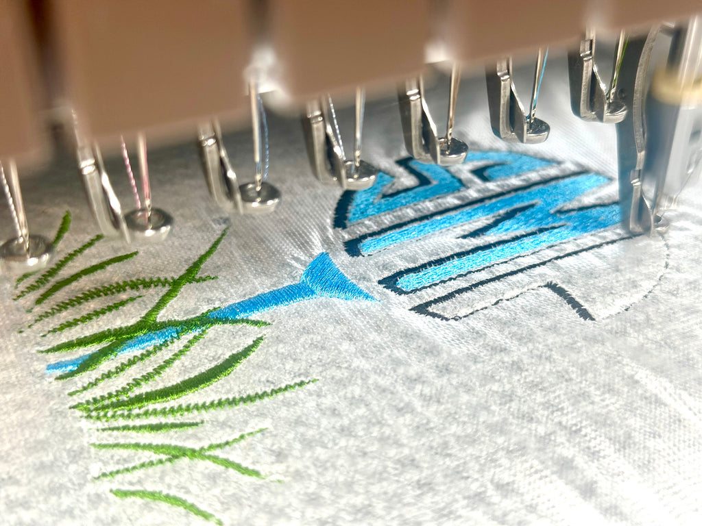 Close up of custom embroidered golf towel in three colors of navy, light blue and green grass.  The monogram is above the golf tee. Waffle weave towel in gray.
