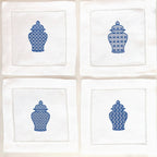 Set of four white linen napkins each with a slightly different chinoiserie design stitched in blue on each. They are set on a white background.
