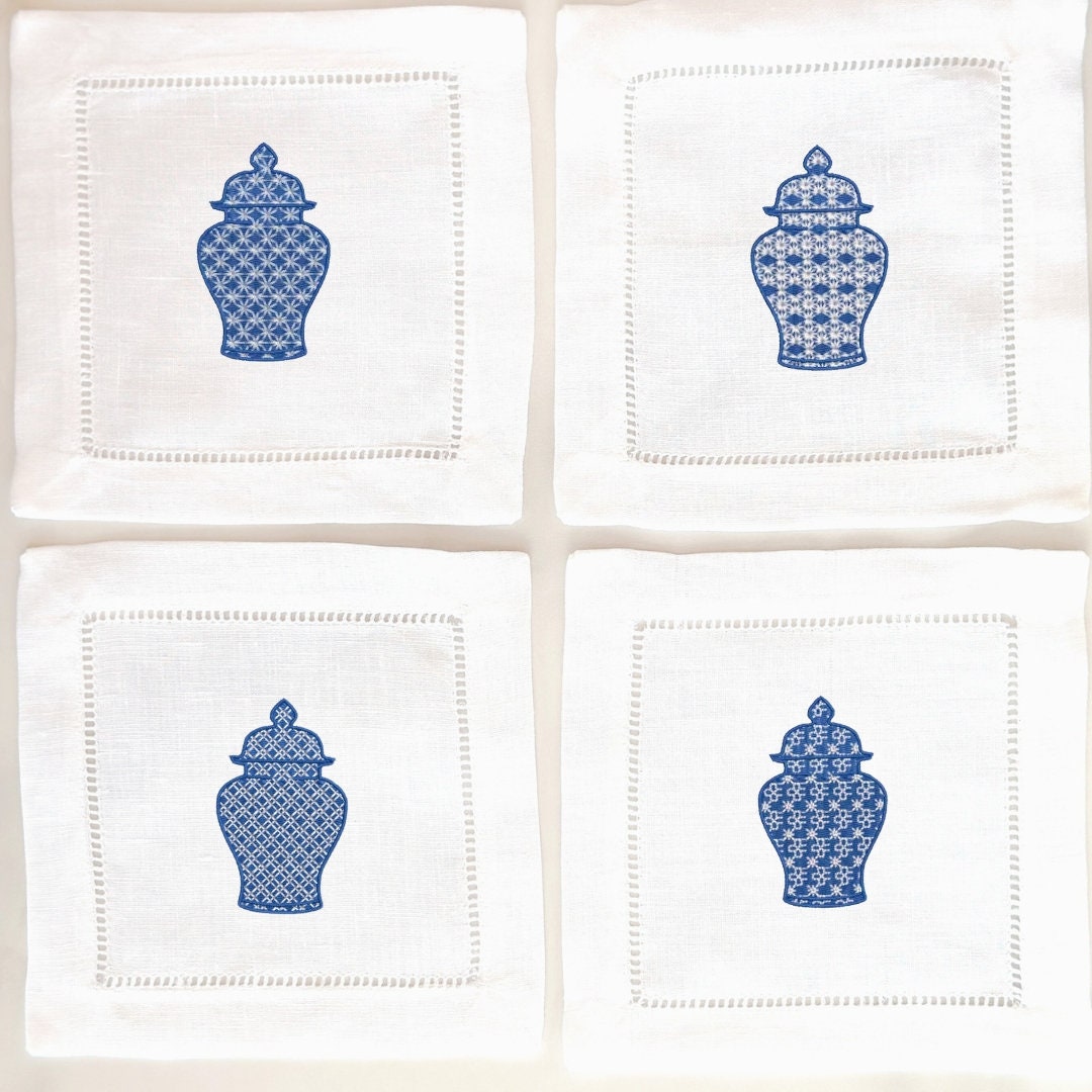 Set of four white linen napkins each with a slightly different chinoiserie design stitched in blue on each. They are set on a white background.