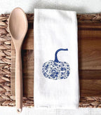 Chinoiserie pattern pumpkin in blue and white on a cutting board with a wooden spoon laid on top of a wicker placemat