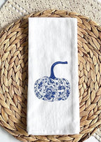 Chinoiserie blue and white pumpkin fall decor embroidered tea towel set on a woven placemat over a crochet throw.
