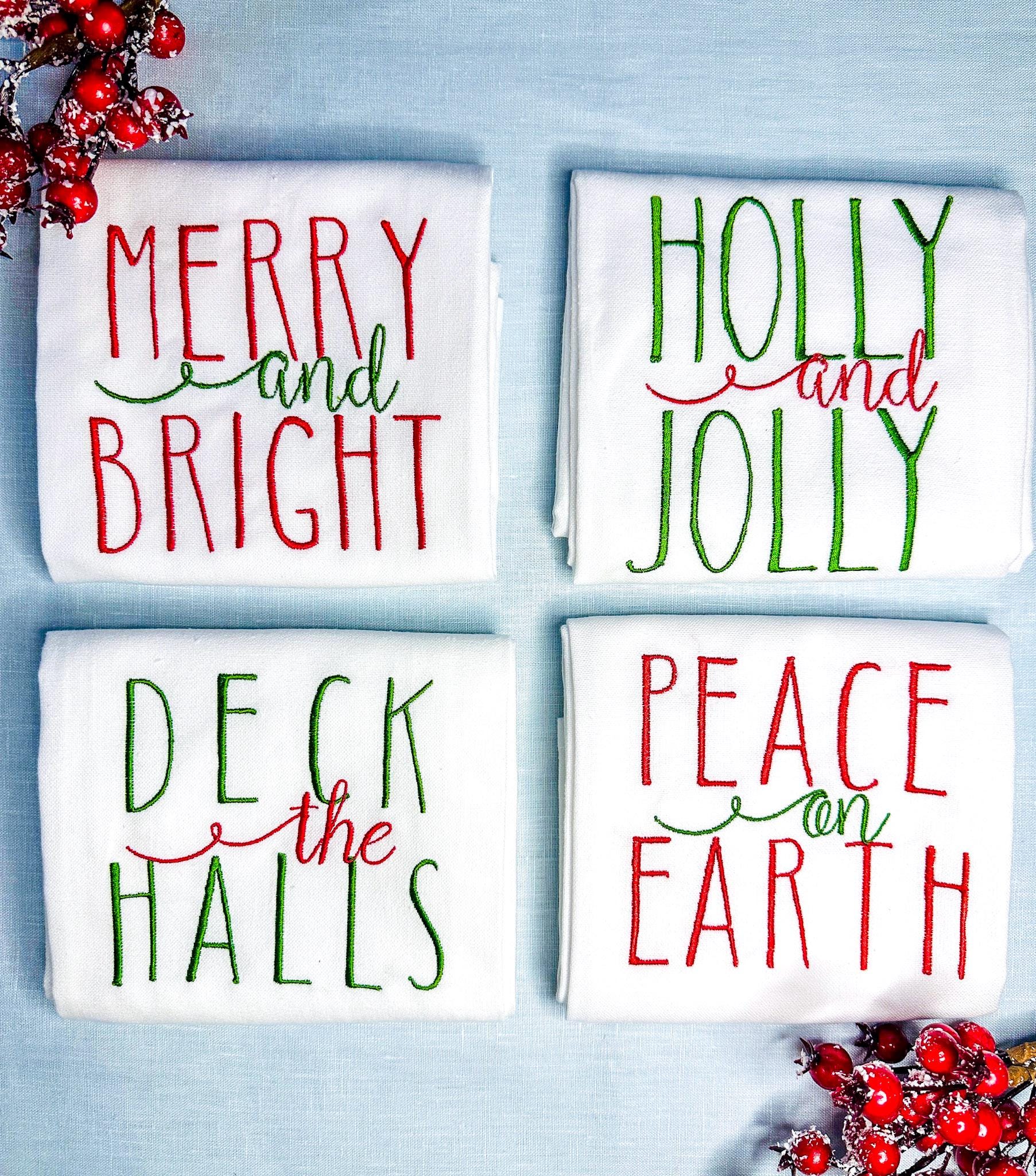 Set of 4 tea towels folded and on a light blue linen tablecloth with red berry branches. Gift for mom in red and green.