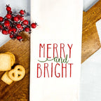 White tea towel on a cutting board with cookies and berry branches embroidered with Merry and Bright as a Secret Santa gift for coworker.