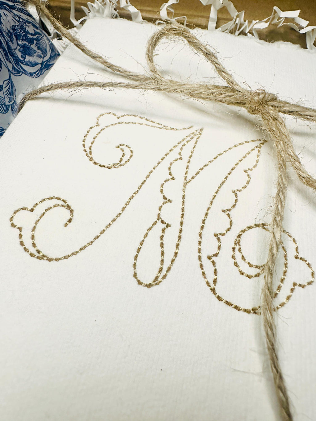 A close up of a custom note card stationery personalized with an initial M tied in twine on chinoiserie blue and white tissue.