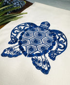 Close up of sea turtle embroidered on white kitchen tea towel with a flower to the left.