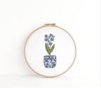 The chinoiserie coquette style pot of flowers embroidered on a white background in a wooden embroidery hoop.
