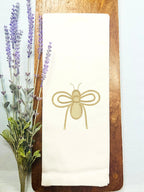 An embroidered bee in gold for bee kitchen decor set on a wooden cutting board with lavender to the left.
