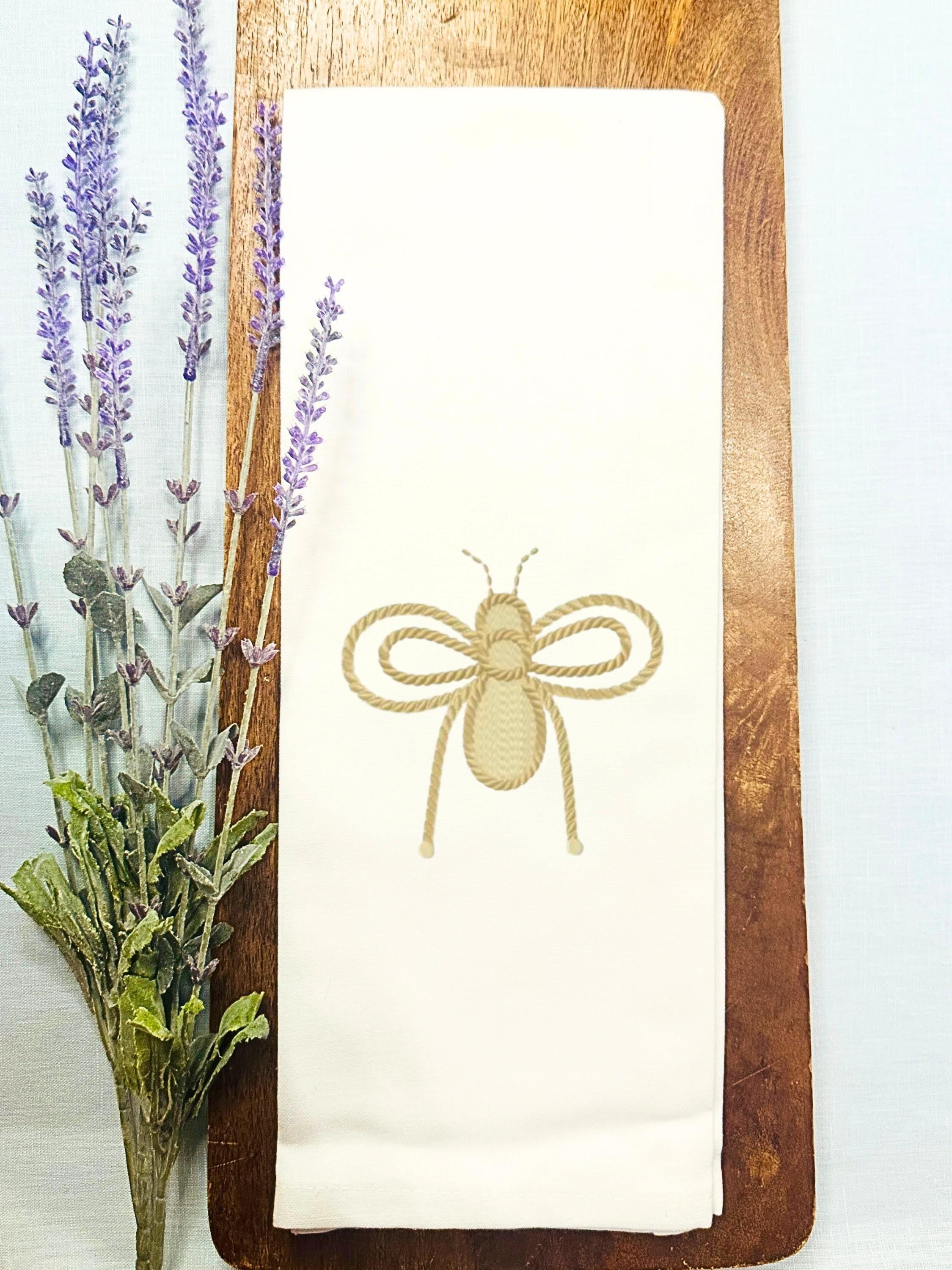 An embroidered bee in gold for bee kitchen decor set on a wooden cutting board with lavender to the left.