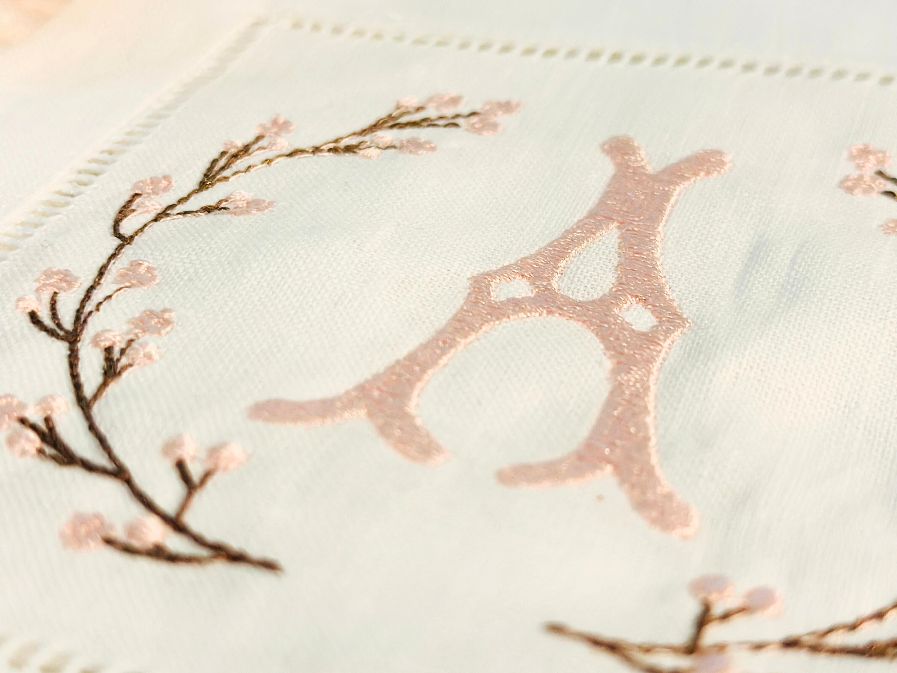 A close up of A set of 4 cocktail napkins embroidered with the letter A in a cherry blossom frame. The cherry blossoms are pink, the stems are brown, and the initial matches the pink of the cherry blossom
