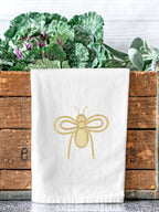 An embroidered gold bee on a white dish towel on the edge of a market bin holding cabbage.