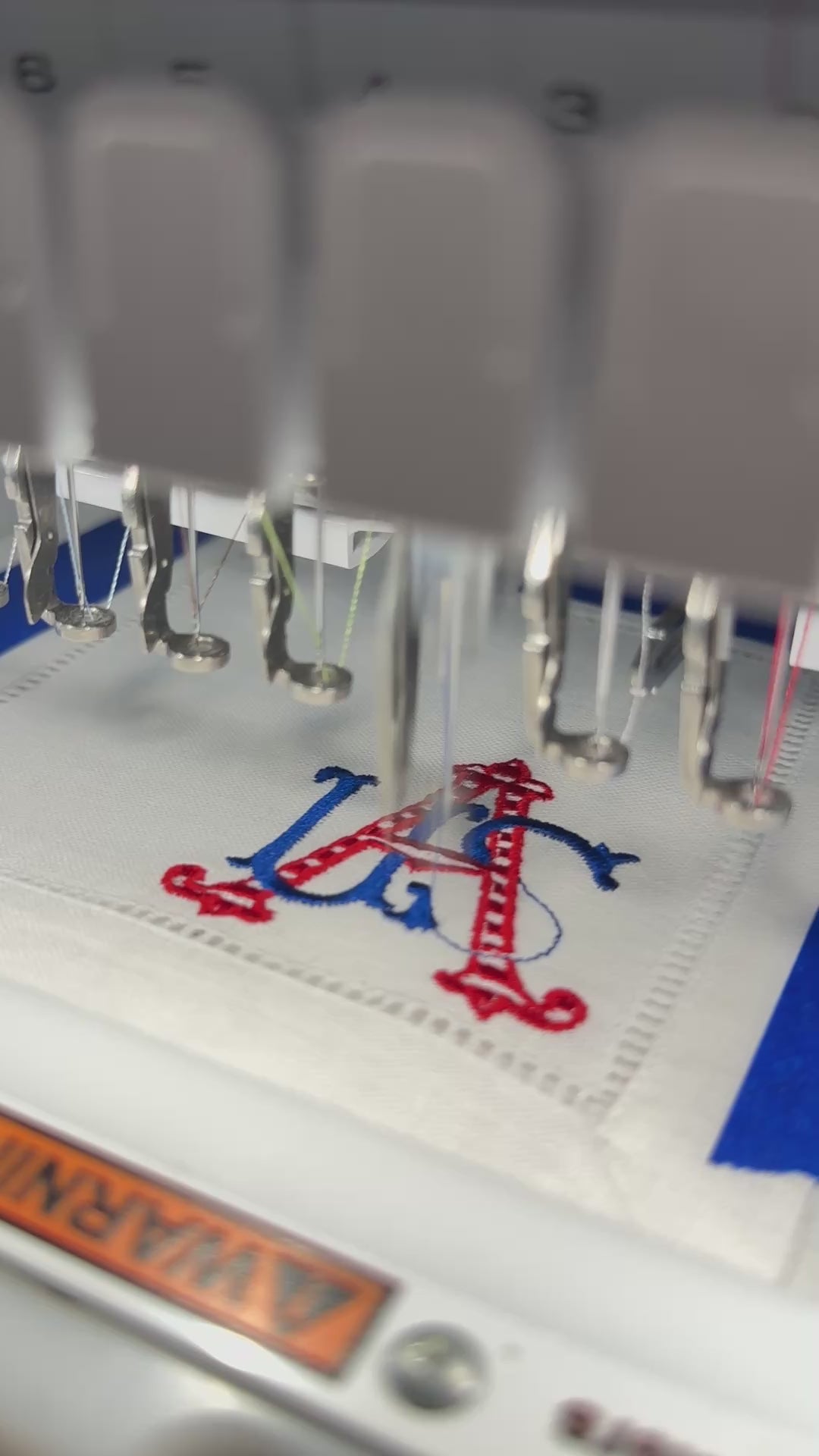 An embroidery machine stitching out USA on a linen cocktail napkin. The design is red and blue.